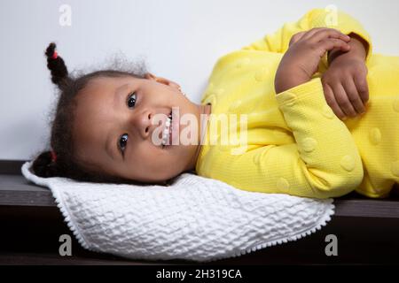 Una bambina afroamericana in abito giallo giace e sorride. Foto Stock