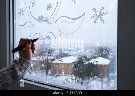 Femmina dipinto a mano cervo di Natale dipinto su vetro della finestra. Decorazioni invernali di Natale sul vetro della finestra. Motivo bianco del cervo. Vento tracciante di arte della neve Foto Stock