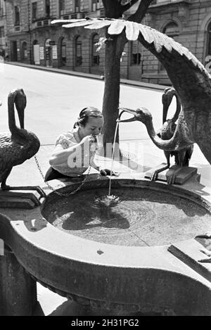 Eine junge Frau probiert das warme Thermalwasser aus dem Reiherbrunnen in der Sophienstraße der Innenstadt von Baden Baden, Deutschland 1930er Jahre. Una giovane donna gusti la calda acqua termale dall'Reiherbrunnen nella Sophienstraße nel centro della città di Baden-Baden, Germania 1930s. Foto Stock