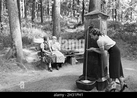 Eine junge Frau probiert das Trinkwasser des Eberbrunnens auf einem Wanderpfad bei Baden-Baden im Nordschwarzwald, Deutschland 1930 Jahre. Una giovane donna sta degustando l'acqua potabile dell'Eberbrunnen su un sentiero escursionistico vicino Baden-Baden nella Foresta Nera del Nord, in Germania anni '30. Foto Stock