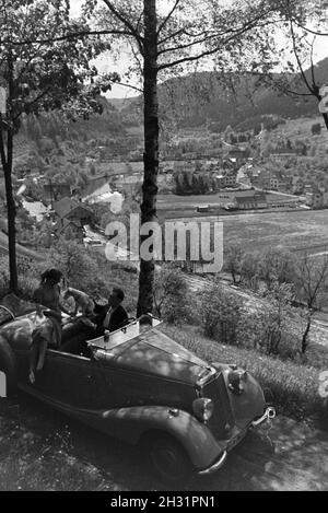 Ein junges Paar und ihr Hund bei einer Spazierfahrt mit dem MERCEDES Cabrio in Hirsau im Nordschwarzwald, Deutschland 1930er Jahre. Una coppia giovane e il loro cane guida attraverso Hirsau nella Foresta Nera settentrionale in una Mercedes cabrio, Germania 1930s. Foto Stock