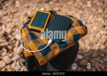 La banca di energia solare carica lo smartphone tramite un cavo USB. Vista dall'alto, primo piano. Ciottoli sullo sfondo. Messa a fuoco soft. Concetto di gadget moderni e rinnovare Foto Stock