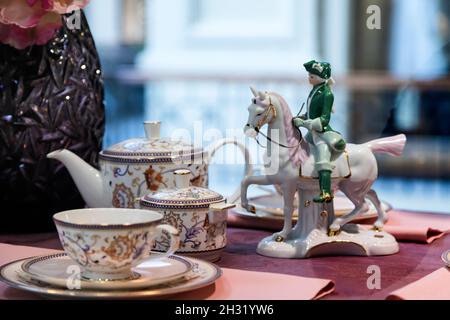 Primo piano elegante set di tè bianco di teiera, ciotola di zucchero e coppia di tè, decorato con fiori sul tavolo e figurine di un cavallo rider Foto Stock