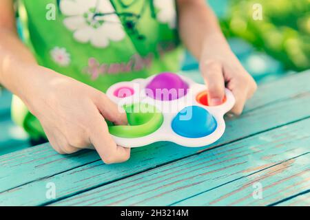 colorato fidget giocattolo antistress sensoriale spingere semplice concavità nelle mani del bambino. La ragazza preme il dito sul giocattolo di gomma pop esso sul tavolo. Foto Stock