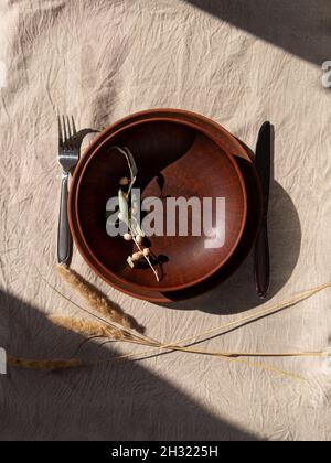 Piatto di argilla artigianale vuoto con coltello a forchetta su tovaglia. Tavolo posto artigianale piatto naturale casa arredamento interno Foto Stock