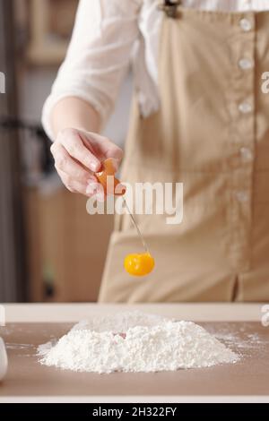 Immagine ravvicinata della donna che mette il tuorlo d'uovo in una pila di farina quando si fa l'impasto per la torta di luna Foto Stock