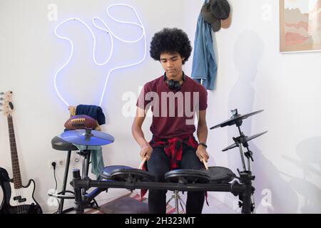 Ragazzo adolescente in casualwear seduto da drumset e battendo sulla batteria durante la ripetizione a casa Foto Stock