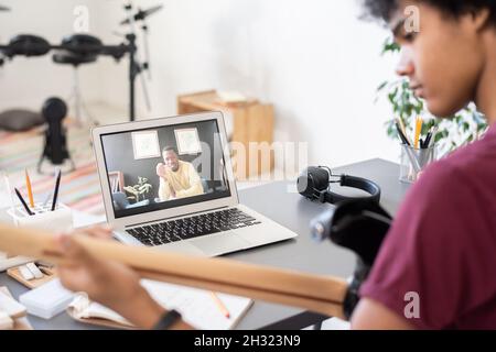 Insegnante di musica fiducioso che consulti ragazzo con la chitarra seduta di fronte al laptop in ambiente domestico durante la lezione online Foto Stock