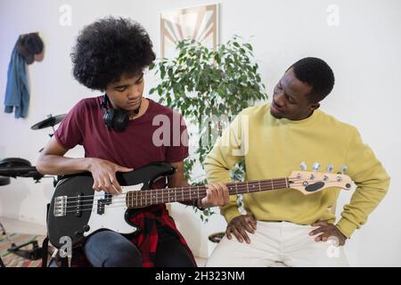 Ragazzo teenage che suona la chitarra mentre il suo insegnante si siede vicino e consultandolo a casa lezione Foto Stock