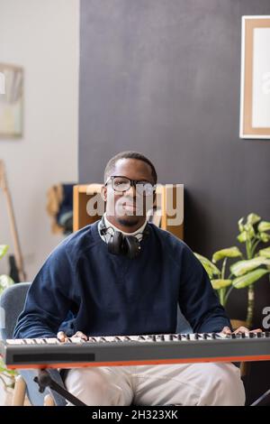 Giovane insegnante di musica seria seduto con la tastiera del pianoforte e guardando voi durante la lezione in studio o a casa Foto Stock