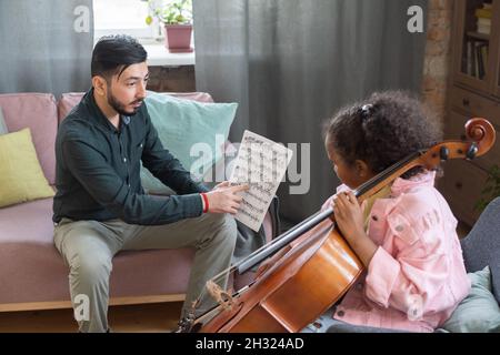 Insegnante di musica fiducioso che punta a carta con note durante la lezione di casa mentre mostra parte di musica al suo allievo Foto Stock