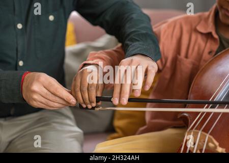 Mani di insegnante di musica e la sua pupilla suonando violoncello mentre il giovane tiene il fiddlestick e aiuta il ragazzino a scivolarlo Foto Stock