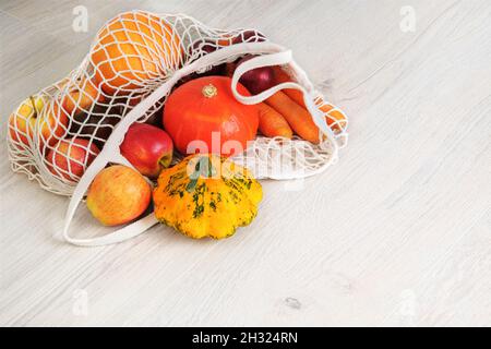 Zucca d'arancia, mele, cipolle, zucchine e carote in sacchetto a rete riutilizzabile naturale. Verdure biologiche che escono dal sacchetto di shopping ecologico. Legno bianco b Foto Stock