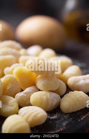 Gnocchi italiani crudi con spinaci su sfondo di legno scuro. Si tratta di gnocchi, solitamente ovali, fatti di pasta di farina di grano con uova Foto Stock