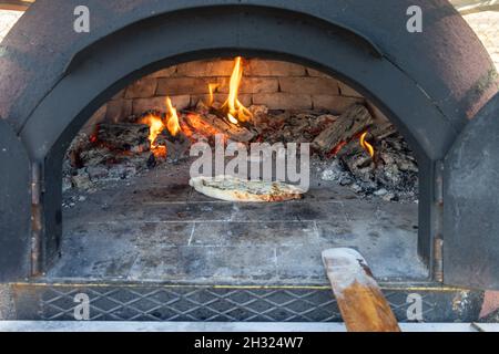 Pita, la pizza sta cucinando in un fuoco di legno in un forno di pietra Foto Stock