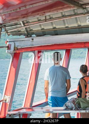 Vista posteriore dei passeggeri amanti che si rilassano sul balcone godendo la vista dalla barca dell'isola di Samui nel mare. Felice coppia di turisti casual fuori su tropicale Foto Stock
