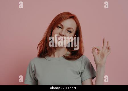 Donna sorridente che le dà approvalwhile posa isolato su sfondo rosa studio Foto Stock