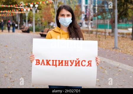 Una donna in una maschera medica tiene un poster con un'iscrizione, tradotto da ucraino ottenere vaccinato Foto Stock