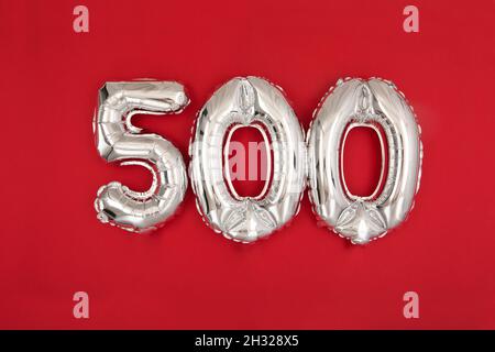 Da sopra di palloncini d'argento lucido che mostrano il numero 500 su sfondo rosso con glitter sparsi Foto Stock