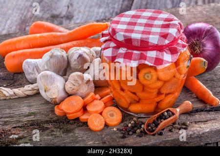 Carota domestica sana in scatola in un vaso e sul vecchio tavolo rustico Foto Stock