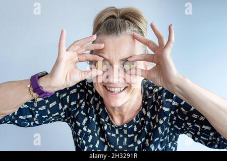 una donna di mezza età smacchiante tiene le monete in euro nelle sue mani vicino ai suoi occhi, primo colpo di testa closeup Foto Stock