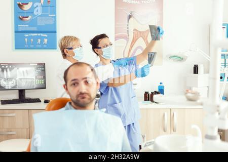 Vista frontale di un malato che guarda la macchina fotografica mentre attende il team medico per esaminare la radiografia somatologica seduto sulla sedia dentale in ospedale ufficio debtal. Stomatologo che fa appuntamento dente Foto Stock