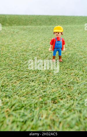 Piccolo giocattolo personaggio contadino Playmobil in piedi in 'campo' di faux / fake erba. Per la produzione di alimenti nel Regno Unito, da azienda agricola a forca, da campo a forca/da campo a piastra. Foto Stock