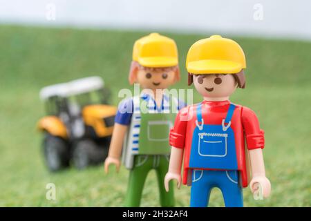 Trattore giocattolo piccolo su erba finta / fake con personaggio contadino Playmobil giocattolo. Per la produzione di alimenti nel Regno Unito, da azienda agricola a forca, da campo a forca/da campo a piastra Foto Stock