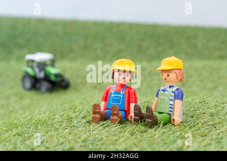 Trattore giocattolo piccolo su erba finta / fake con personaggio contadino Playmobil giocattolo. Per la produzione di alimenti nel Regno Unito, da azienda agricola a forca, da campo a forca/da campo a piastra Foto Stock