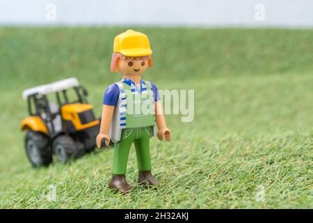 Trattore giocattolo piccolo su erba finta / fake con personaggio contadino Playmobil giocattolo. Per la produzione di alimenti nel Regno Unito, da azienda agricola a forca, da campo a forca/da campo a piastra Foto Stock
