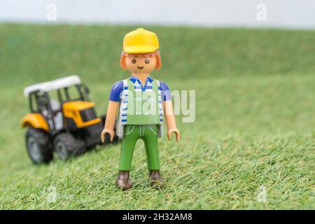 Trattore giocattolo piccolo su erba finta / fake con personaggio contadino Playmobil giocattolo. Per la produzione di alimenti nel Regno Unito, da azienda agricola a forca, da campo a forca/da campo a piastra Foto Stock