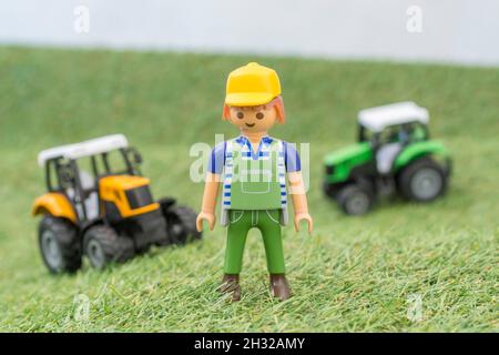 Trattore giocattolo piccolo su erba finta / fake con personaggio contadino Playmobil giocattolo. Per la produzione di alimenti nel Regno Unito, da azienda agricola a forca, da campo a forca/da campo a piastra Foto Stock