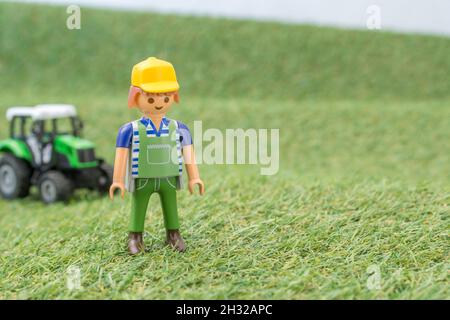 Trattore giocattolo piccolo su erba finta / fake con personaggio contadino Playmobil giocattolo. Per la produzione di alimenti nel Regno Unito, da azienda agricola a forca, da campo a forca/da campo a piastra Foto Stock