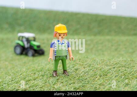 Trattore giocattolo piccolo su erba finta / fake con personaggio contadino Playmobil giocattolo. Per la produzione di alimenti nel Regno Unito, da azienda agricola a forca, da campo a forca/da campo a piastra Foto Stock