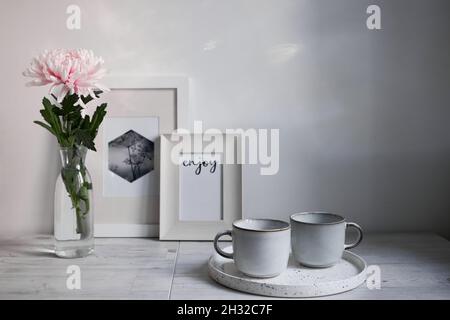 Stile Scandinavo. Design degli interni. Grande crisantemo rosa in un lungo vaso di vetro. Due tazze di dimensioni diverse. Cornice per foto. Spazio vuoto per il testo Foto Stock