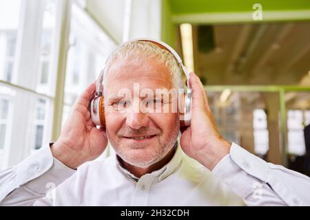Uomo anziano con cuffie durante l'ascolto di musica in streaming o durante una videoconferenza Foto Stock