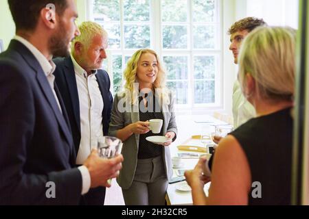 Gruppo di uomini d'affari che hanno un piccolo colloquio durante la pausa caffè dopo una riunione Foto Stock