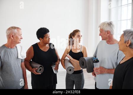 Gruppo di anziani con tappetini che parlano con il loro allenatore dopo lezioni di yoga in studio Foto Stock