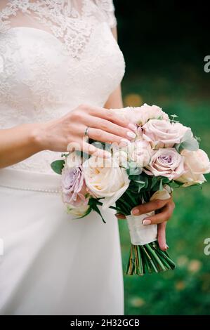 Cerimonia nuziale all'aperto. Giovane sposa caucasica in abito in pizzo bianco per un bouquet nuziale di rose fresche e peonie da vicino. Foto Stock