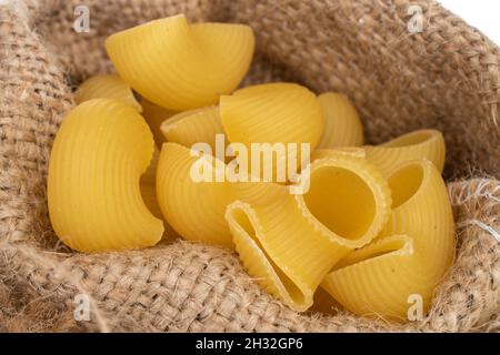 Pasta cruda giallo brillante in sacchetto di iuta, primo piano, isolato su bianco. Foto Stock