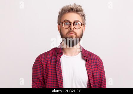 Ritratto di scioccato da notizie bearded uomo freelancer in occhiali e camicia a scacchi sorprendentemente guardando la macchina fotografica. Studio interno girato isolato su sfondo grigio Foto Stock