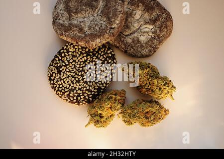 La marijuana fiorisce e dolci isolati su sfondo bianco. Fiori di cannabis e biscotti da vicino. Illuminato dalla luce del sole. Canapa ricreazione, canna kitch Foto Stock