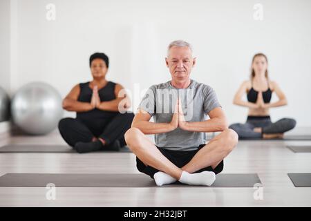 Ritratto di uomo anziano seduto in posizione lotus e meditando durante la lezione di yoga in studio Foto Stock