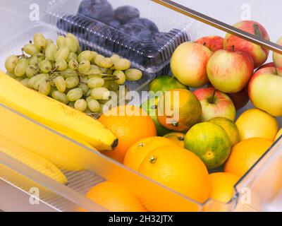 Un cassetto frigorifero pieno di frutta (arance, mandarini, uva, banane, mele, prugne). Foto Stock