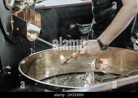 Uomo che versa i chicchi di caffè nella macchina tostatrice Foto Stock