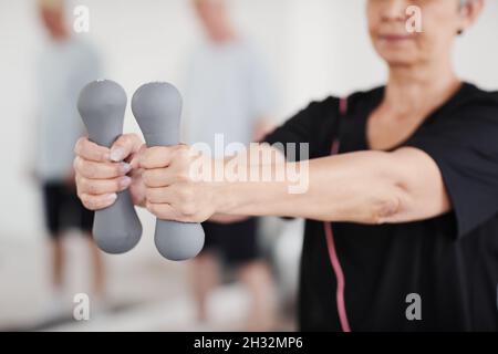 Primo piano della donna anziana che allunga le braccia con manubri mentre fa gli esercizi in palestra Foto Stock