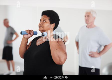 Donna mature plump sollevamento manubri mentre si allenano insieme ad altre persone in palestra Foto Stock