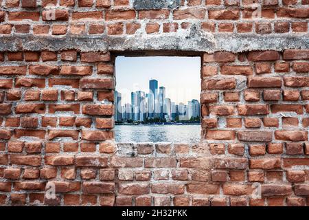 Vecchio muro di mattoni in rovina con vista sul mare e sui grattacieli. Concetto di urbanizzazione. Foto Stock