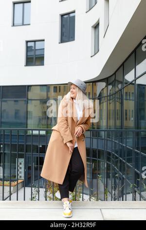 giovane donna bionda in un cappotto beige e cappello sorridente Foto Stock