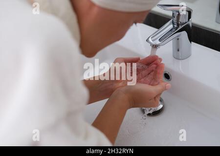 Donna in accappatoio lava il viso con acqua pulita Foto Stock